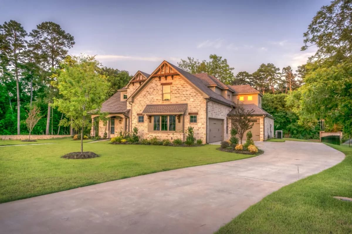 A stone-clad custom home at dusk with a sweeping driveway
